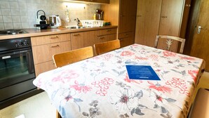 A kitchen with wooden cabinets, a stove, and a sink. There is a table with a floral tablecloth and a chair. - Bürcher Haus 1. OG Süd-West by Interhome (Riederalp)