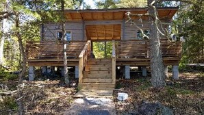 Eine rustikale Holzhütte mit einer Holzterrasse, einer zentralen Treppe und einer natürlichen Umgebung.