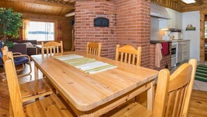 Una mesa de comedor de madera con sillas, una chimenea de ladrillo y una zona de cocina con armarios y un lavamanos.