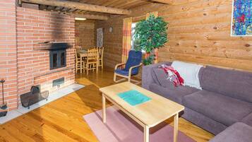 A cozy living room with a brick fireplace, wooden furniture, and a large plant.