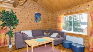 Interior acogedor de una cabaña con pared de troncos de madera, un sofá gris, una mesa de centro de madera y un ventanal con cortinas.