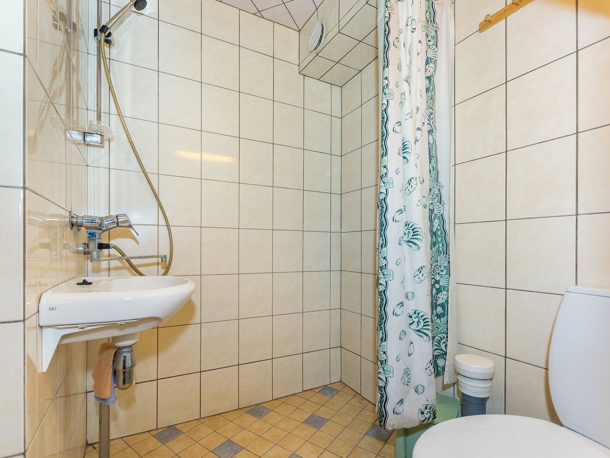 Un baño con un lavamanos blanco, una ducha con cortina de baño verde y blanca, y un inodoro.