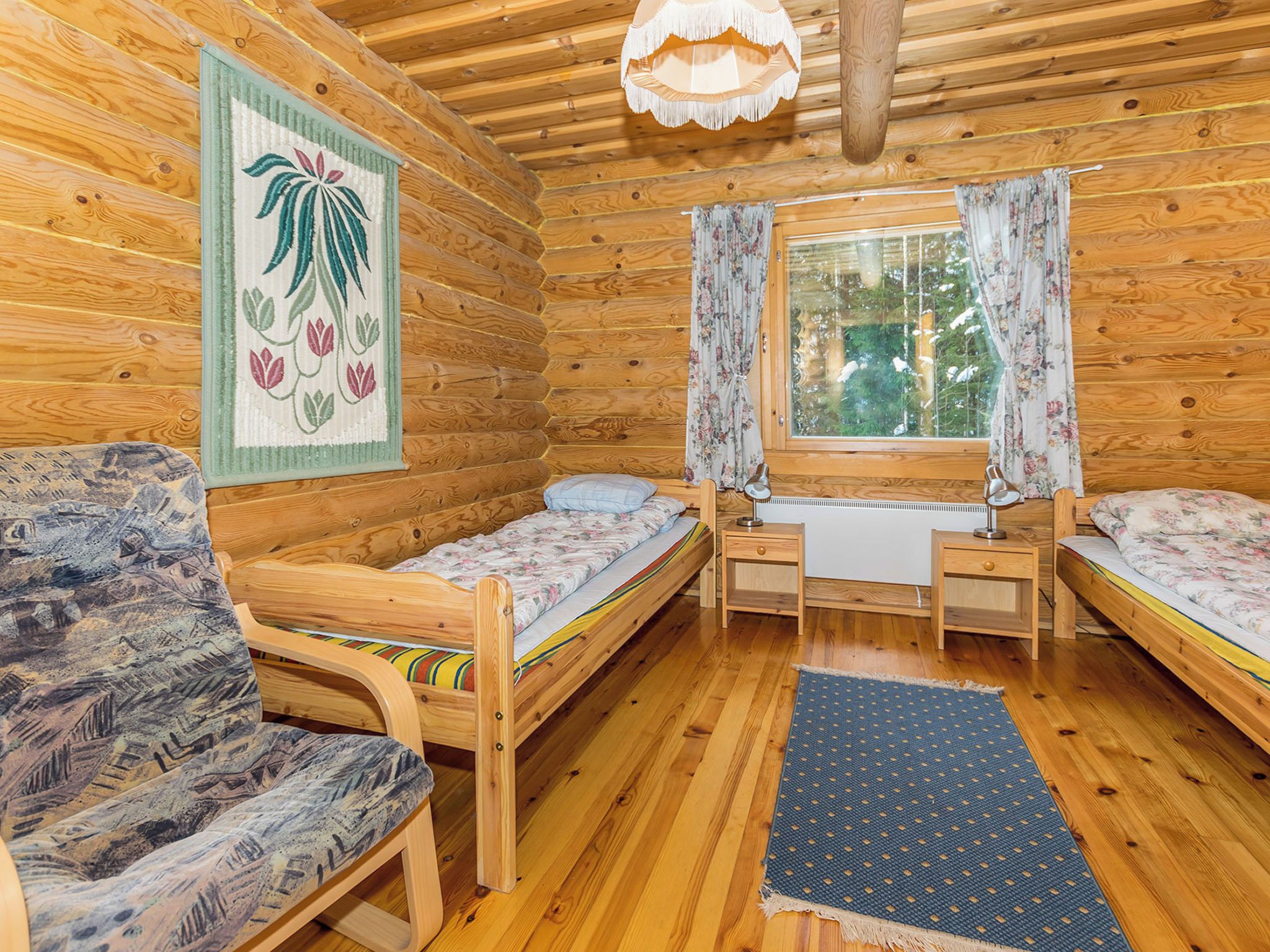 Interior acolhedor de uma cabana, com decoração em madeira, duas camas de solteiro, um sofá e uma mesa com duas cadeiras.