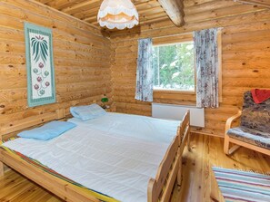 Una habitación de cabaña de madera con una cama, una ventana con cortinas, una lámpara y una silla.
