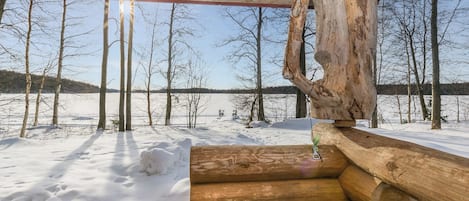 A wooden cabin with a view of a snowy landscape and a body of water.