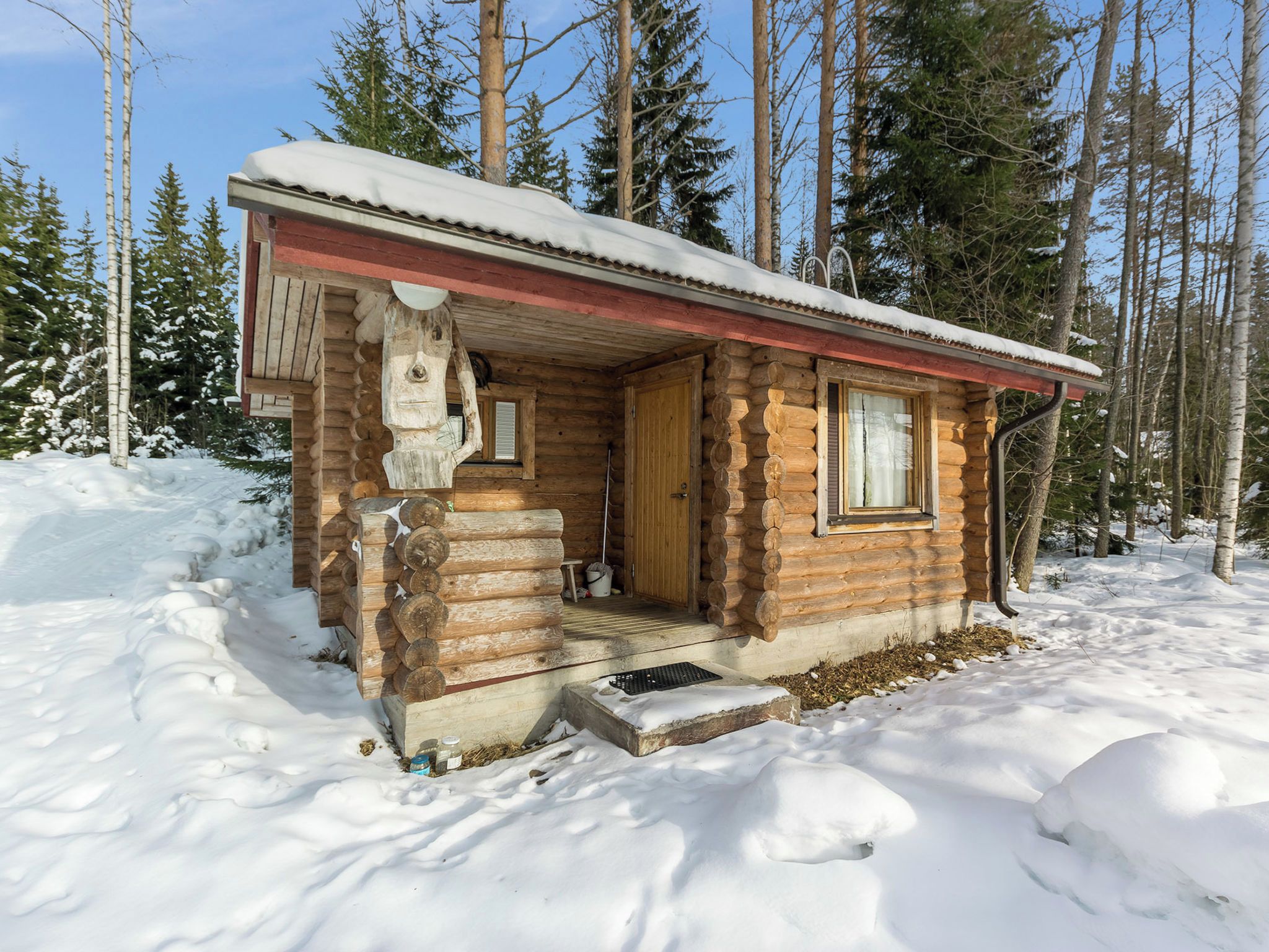 Hirsimökki, jossa on puinen kuisti, ovi ja ikkuna.