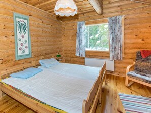 A wooden cabin room with a bed, a chair, a window with curtains, and a hanging light fixture.
