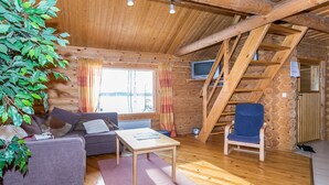 Un interior de cabaña acogedor, con techo de madera, un sofá, una silla, una mesita y un televisor.