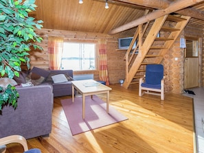 A cozy cabin interior with a sofa, a table, a chair, a TV, and a staircase.