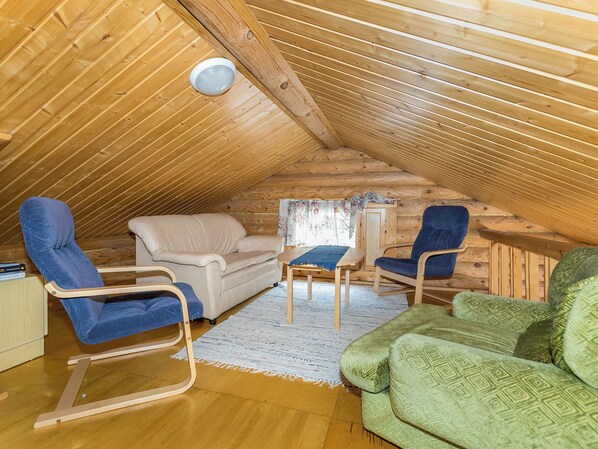 An attic room with a sloped ceiling, a beige sofa, a blue chair, a green sofa, and a small table with a blue tablecloth.