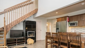 Un espacio habitable moderno con una escalera de madera, un televisor de pantalla plana, una zona de comedor con sillas de madera y una cocina con microondas.