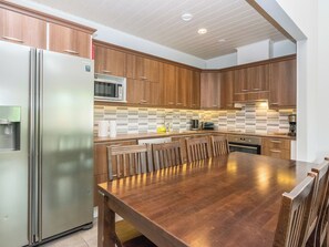 Una cocina moderna con armarios de madera, un refrigerador de acero inoxidable, un microondas y un comedor con mesa y sillas de madera.