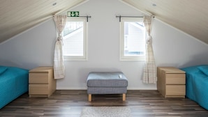 Una habitación con techo inclinado, dos ventanas con cortinas, un banco y dos mesitas de noche.