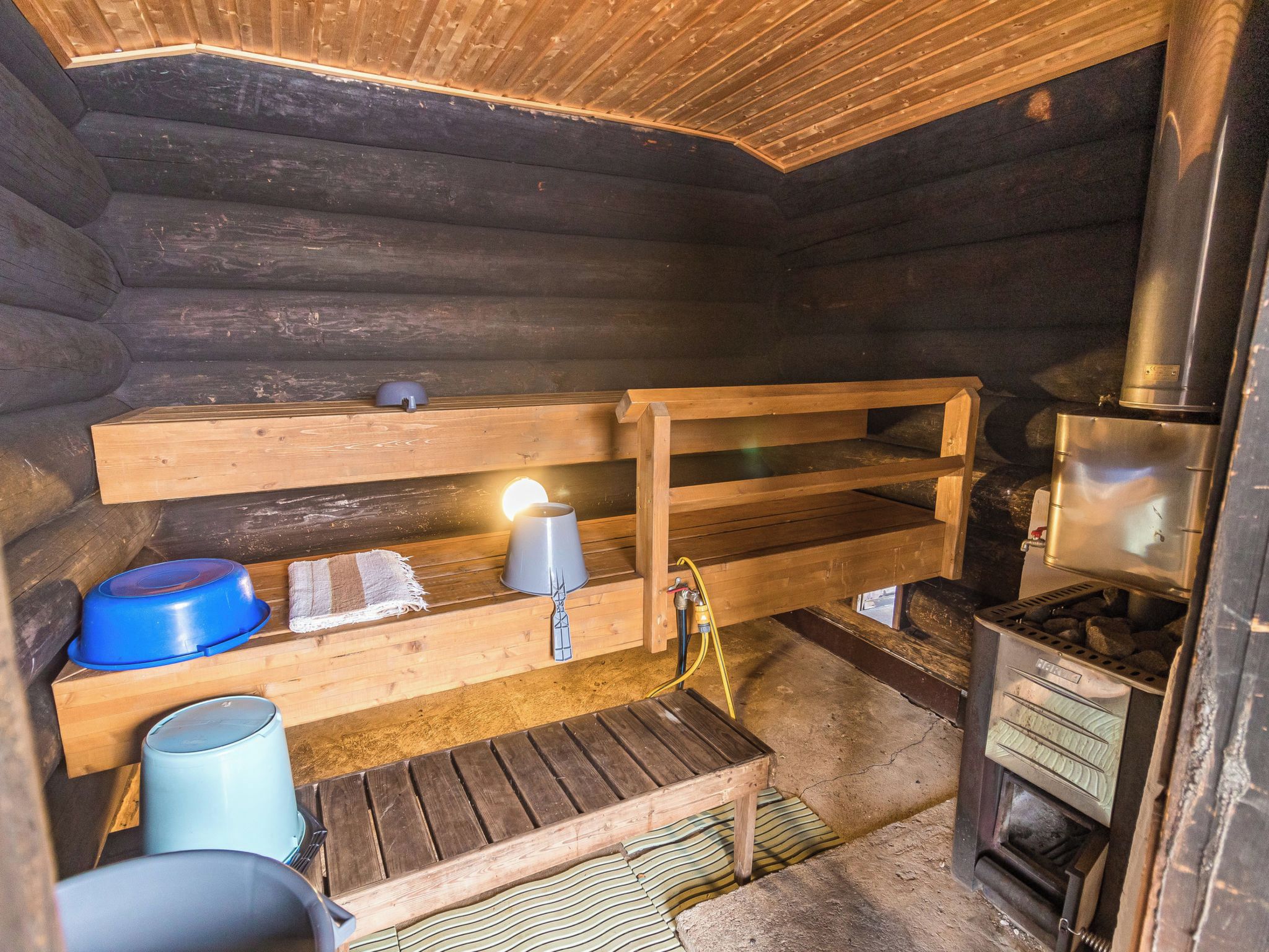 A rustic cabin interior with a wooden bench, a stove, and various containers.
