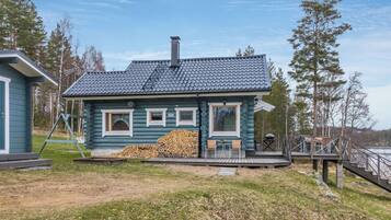 Eine Blockhütte mit Schornstein, einer Veranda und einem Holzstapel.