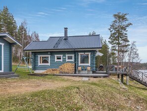 A log cabin with a chimney, a deck, and a stack of firewood.