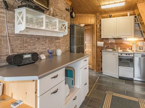 A kitchen with a brick wall, white cabinets, a built-in stove, and a coffee maker.