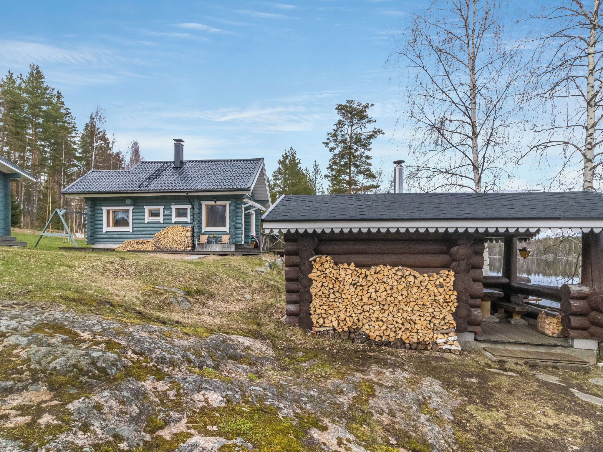 A log cabin with a deck and a small wooden structure with a roof.