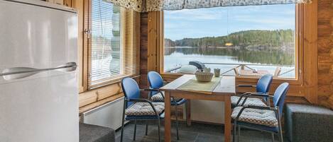 Een chalet van binnen met een eettafel, stoelen, een koelkast en uitzicht op een meer.