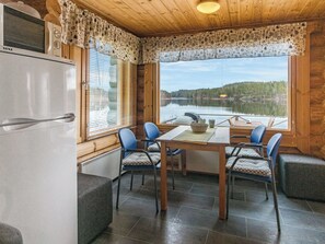 L’intérieur d’une cabane comprenant une table à manger, des chaises, un réfrigérateur et une vue sur un lac.