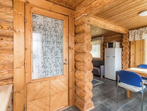 A wooden cabin interior with a dining area, kitchen, and a door with a bamboo pattern.