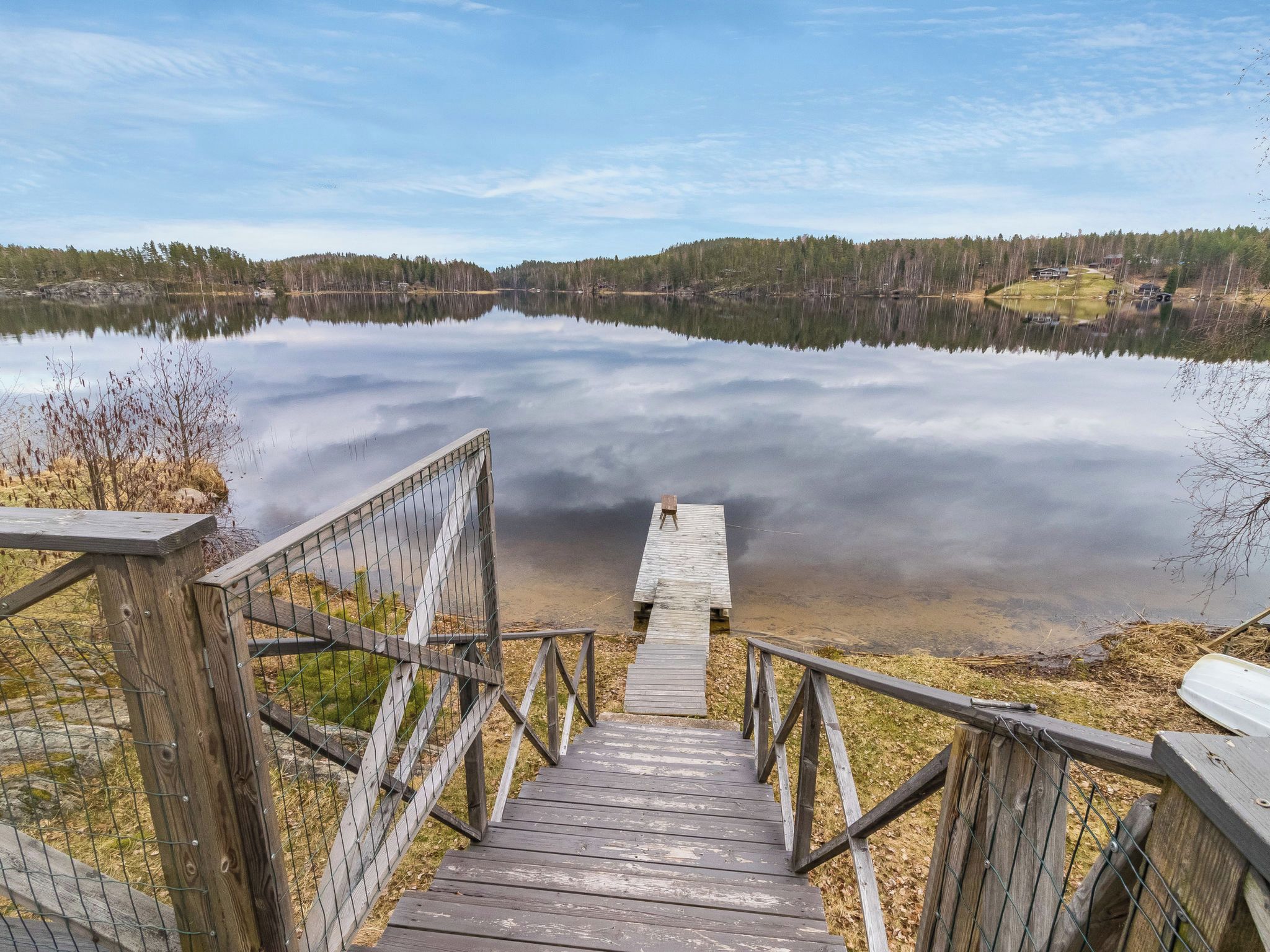 A wooden staircase leading to a dock over a calm lake, surrounded by trees and a clear sky.