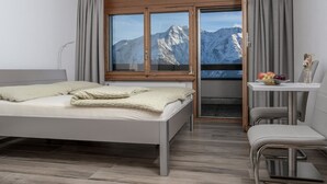 Een moderne hotelkamer met een bed, een bureau en uitzicht op bergen door een groot raam.
