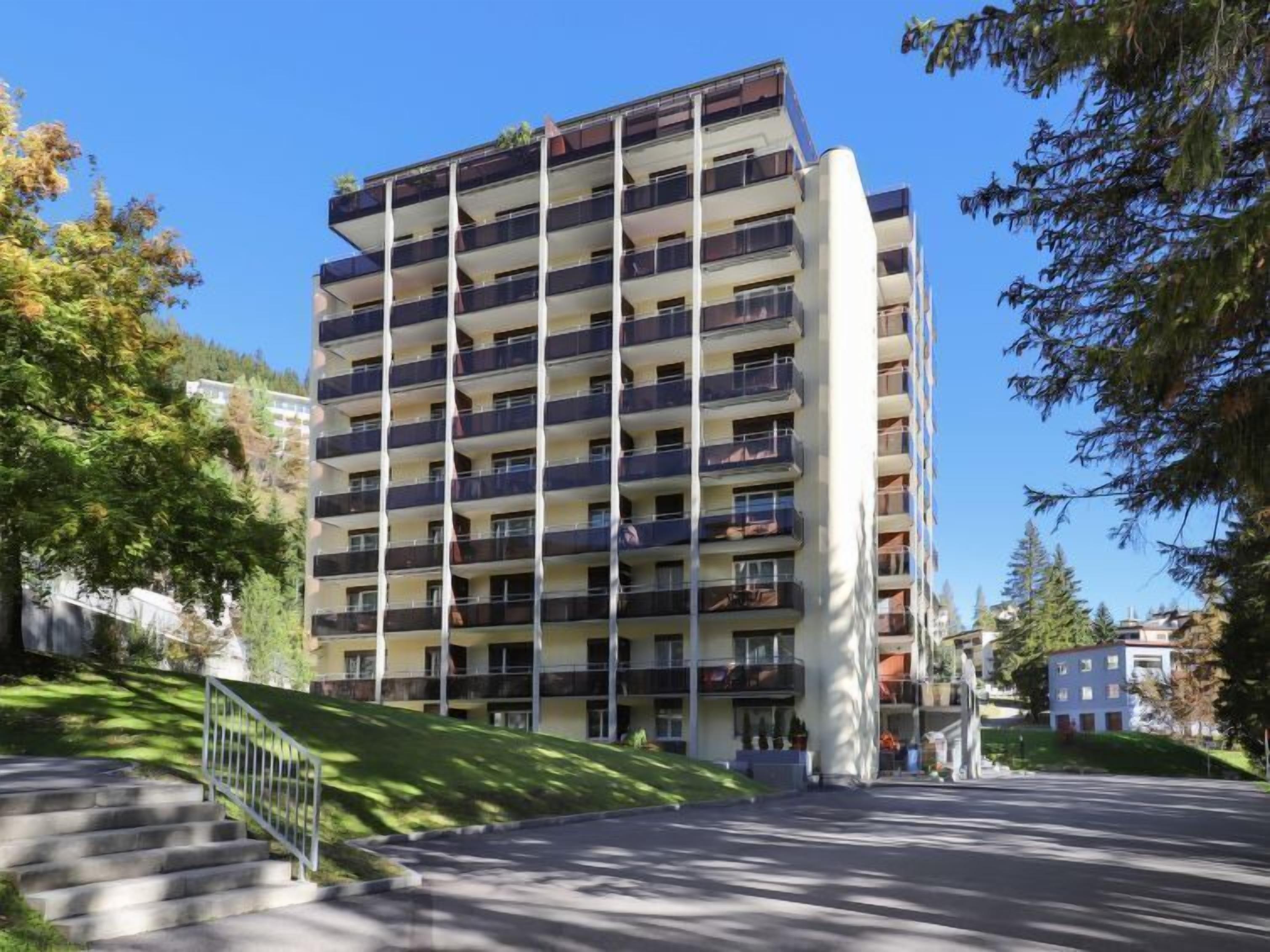 Un edificio residencial de varios pisos con balcones, una escalera que lleva a la entrada y un cielo despejado.