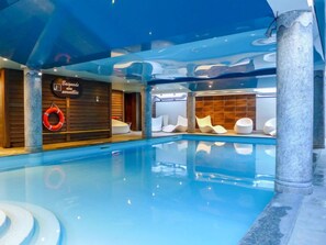 A modern indoor swimming pool with a clear water surface, surrounded by stone pillars and wooden walls. - Ginabelle 1 by Interhome (Chamonix)