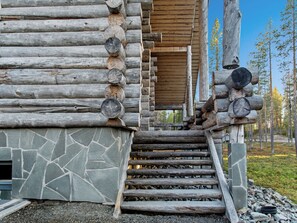 A log cabin with a stone foundation, wooden steps leading to a wooden door, and a clear sky in the background.