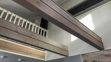 A multi-level interior with exposed wooden beams, a stone accent wall, and a staircase.