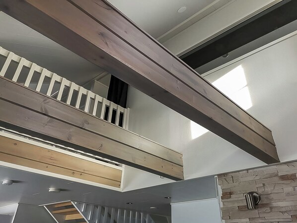 A multi-level interior with exposed wooden beams, a stone accent wall, and a staircase.