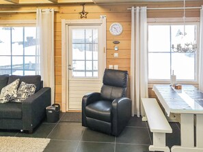 A room with a black leather chair, a sofa with patterned cushions, a wooden door, and a dining table with a bench.