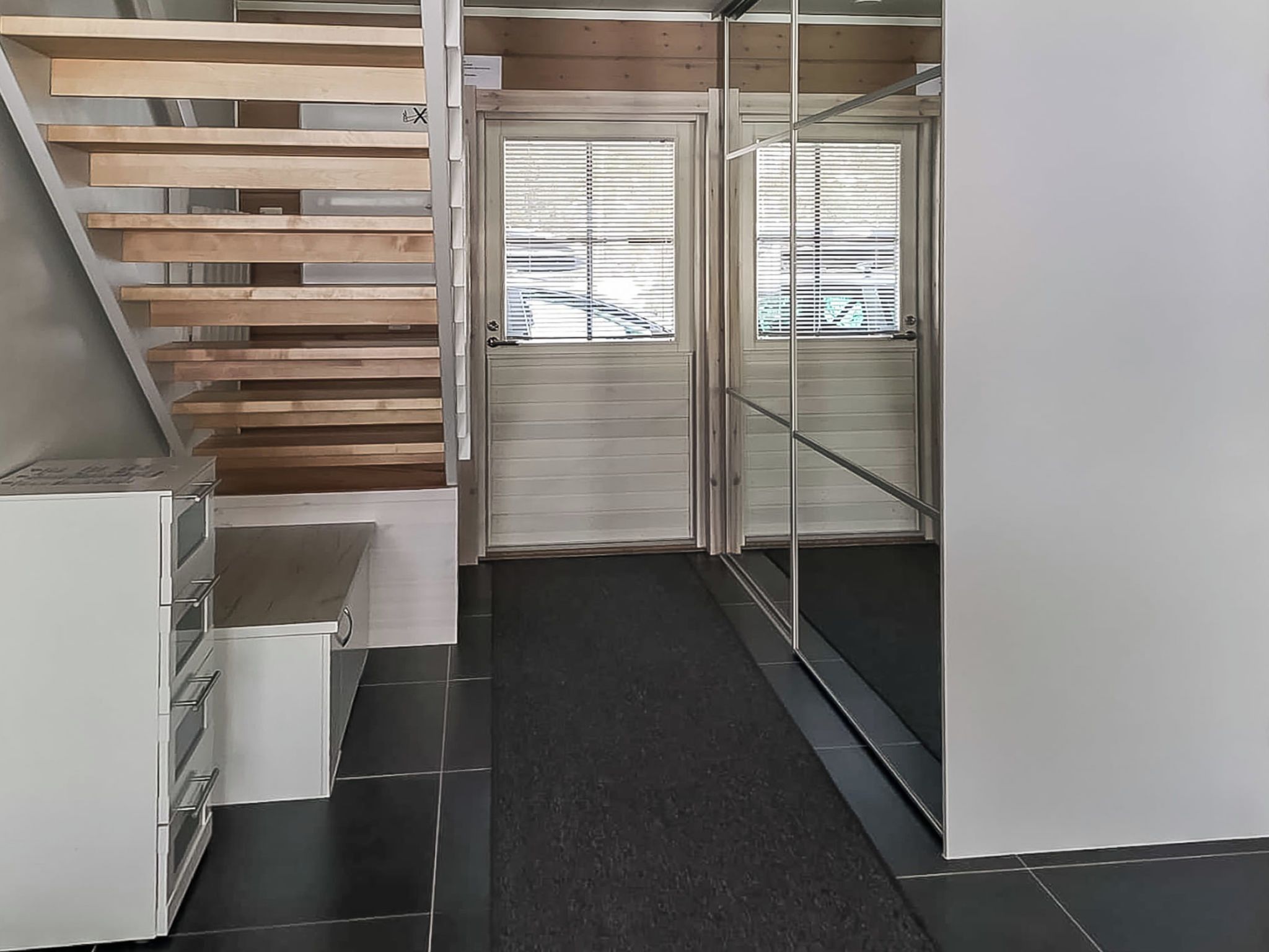 A modern interior with a staircase, a door with a window, and a tiled floor.