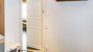 Una habitación con una puerta blanca, un banco y un televisor montado en la pared.