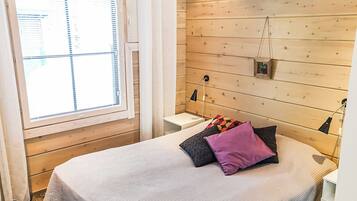 Ein Schlafzimmer mit einem Bett, einem Fenster mit Jalousien, einem Nachttisch und einer Wandlampe.