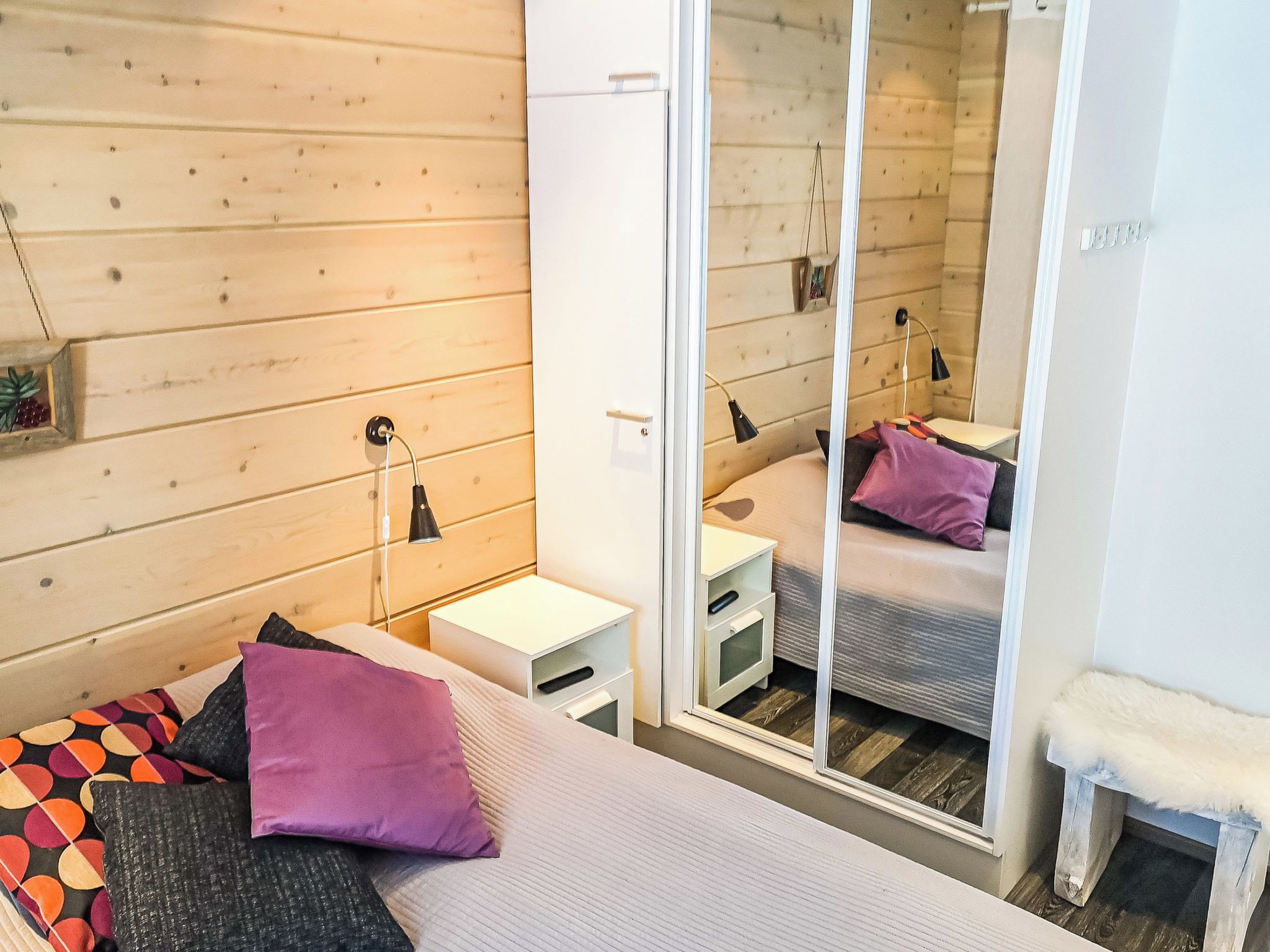 Une chambre à coucher avec un lit, une table de chevet, une lampe, un miroir et un petit tabouret blanc.