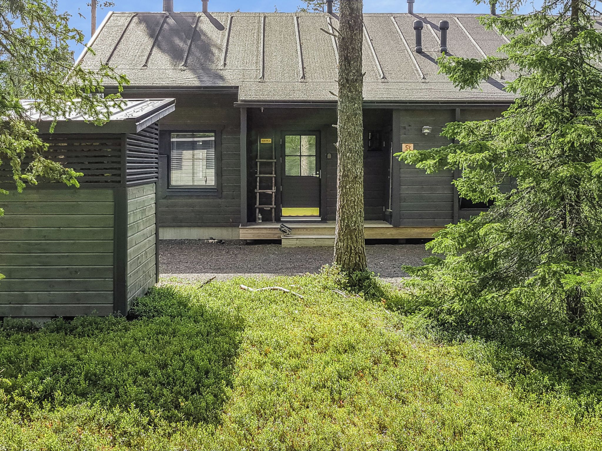 Une maison moderne à deux étages, avec une façade sombre, un porche à l’avant et un petit jardin devant.