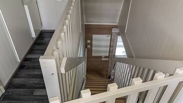 A staircase with a wooden finish and white railings, leading to a landing with a door and a window.