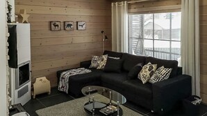 Una sala de estar moderna con un sofá seccional negro, una mesa de centro de vidrio y una pared de madera decorada con motivos de animales.