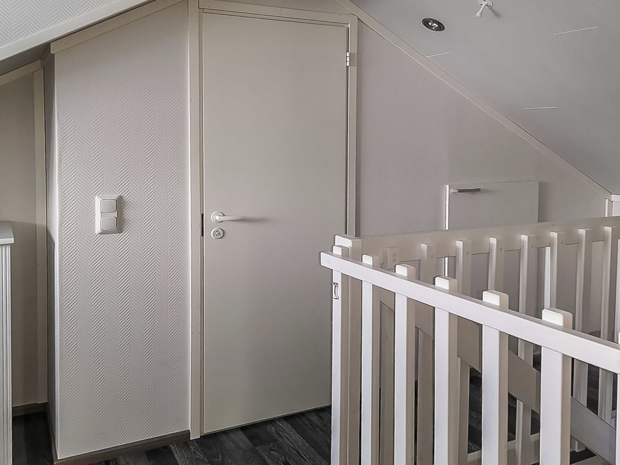Un couloir avec une porte fermée, une rambarde blanche et un mur à texture.