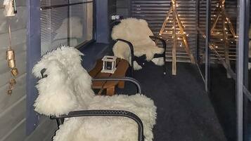 A room with a fur-covered chair, a small table with a box, and a wooden ladder structure with lights.
