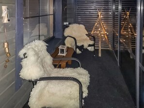 Een kamer met een fauteuil bekleed met vacht, een klein tafeltje met een doos, en een houten constructie met een ladder en verlichting.