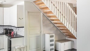 Una cocina moderna con armarios blancos, estufa integrada y una escalera de madera.