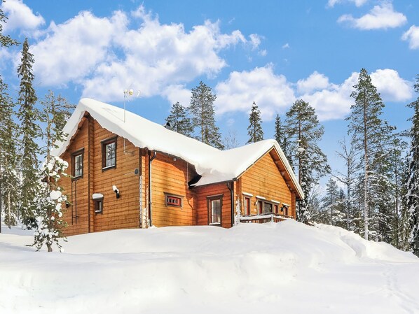 A wooden cabin with a snow-covered roof, surrounded by tall pine trees. - Tervakko by Interhome (Sodankylä)