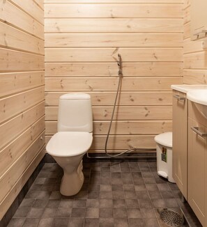 A small, wooden-paneled bathroom with a toilet, a bidet, and a sink. - Tervakko by Interhome (Sodankylä)