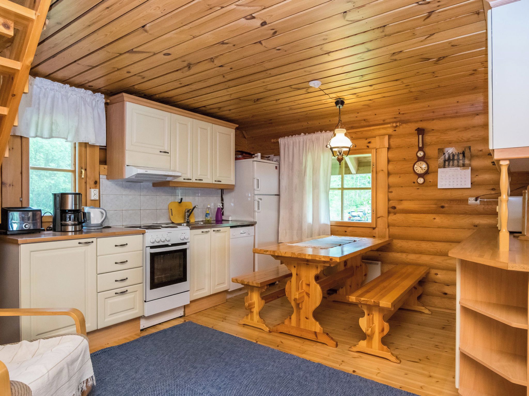 Una cucina compatta con mobili bianchi, un fornello, un frigorifero e un tavolo da pranzo in legno con panche.