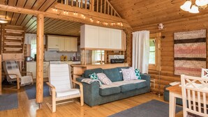 Interior acogedor de una cabaña con techo de madera, zona de comedor, sofá y cocina.