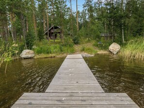 Puinen laituri, joka johtaa metsän ympäröimään mökkiin.