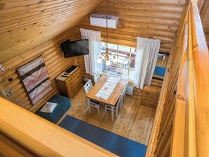 Een knus cabin interieur met een houten vloer, een eettafel met stoelen, een aan de muur bevestigde televisie en een raam met gordijnen.